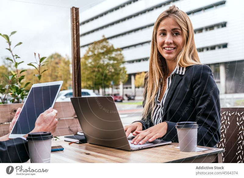 Positiv eingestellte Frau, die in der Nähe eines gesichtslosen Kollegen am Laptop sitzt Geschäftsfrau Café Terrasse Tablette online Browsen Mitarbeiterin Arbeit