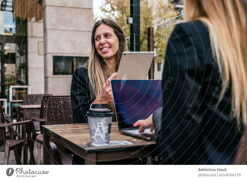 Fröhliche Geschäftsfrau in der Nähe eines gesichtslosen Mitarbeiters am Tisch mit Gadgets Geschäftsfrauen Café Terrasse Tablette Laptop online Browsen