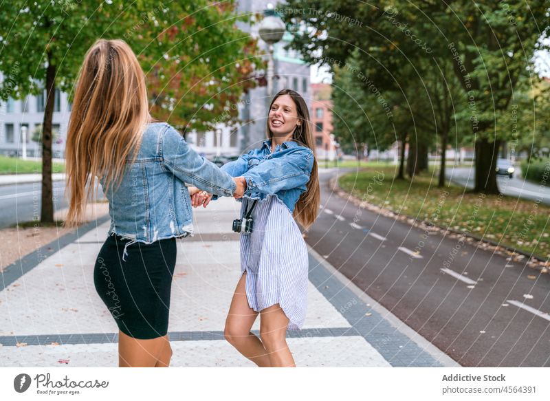 Zufriedene Frauen, die sich auf der Straße drehen Freund Fotoapparat sich im Kreise drehen sorgenfrei Spaß haben Zeit verbringen Hobby Großstadt positiv heiter