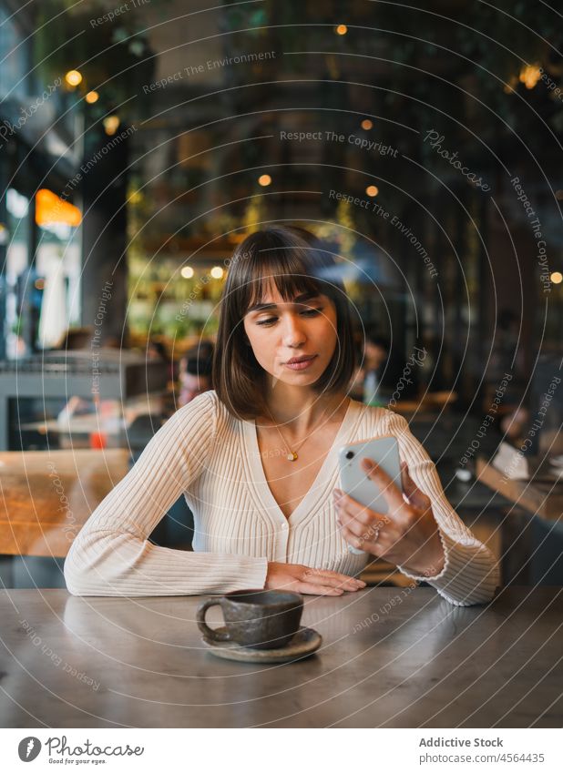 Junge Frau prüft in einem Café Nachrichten auf ihrem Smartphone Kaffee Talkrunde Tasse benutzend trinken Mobile Apparatur Gerät online Anschluss Telefon