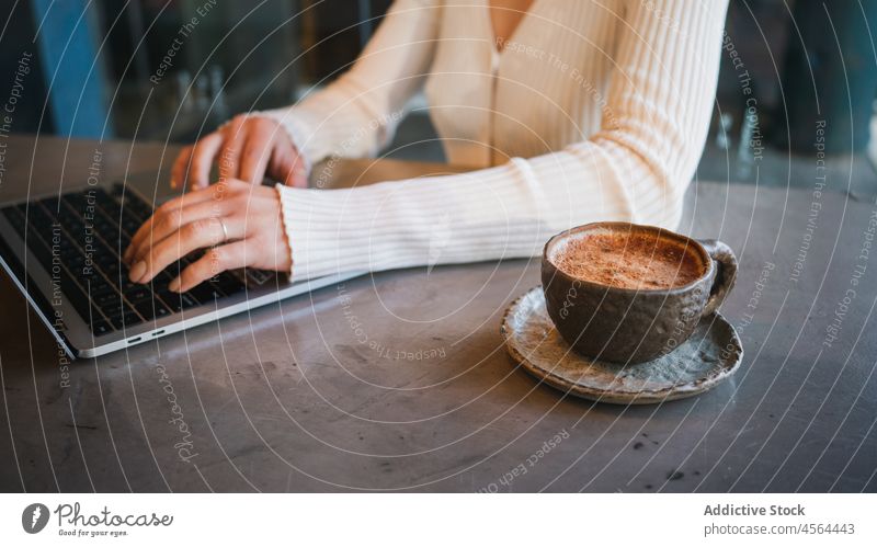 Eine Tasse Cappuccino steht auf dem Tisch neben einer Frau mit Laptop lecker Kaffee Apparatur trinken Tippen geschmackvoll benutzend freiberuflich Browsen Café