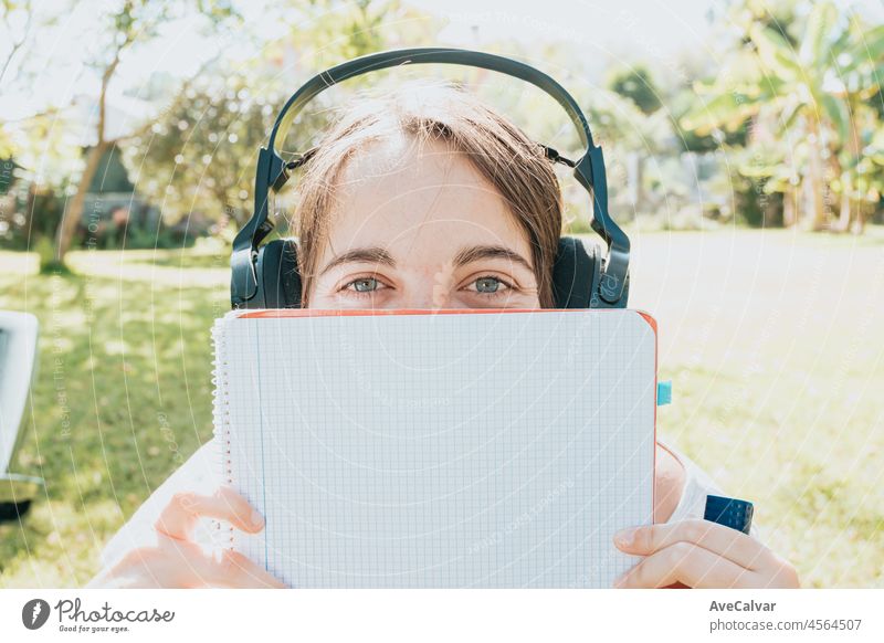 Junge Frau, die im Garten sitzt und lächelt und für die Universität studiert, genießt die Erholung im Freien, hört Musik und benutzt einen Laptop. Kopieren Raum, Menschen Lebensstil Konzept. Tippen auf dem Computer