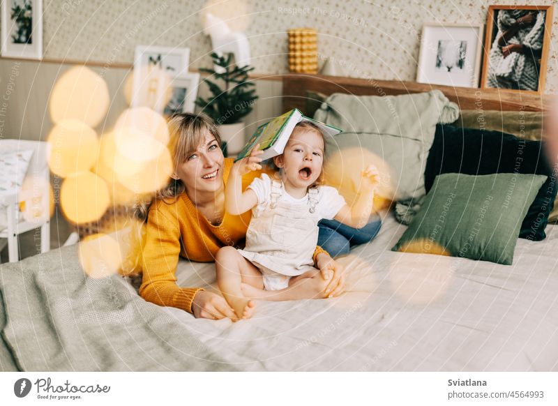 Mutter und Tochter lesen ein Buch und lächeln, sie sitzen zu Hause auf dem Bett. Neujahr, Weihnachten, Familie, gemeinsame Zeit Mama Weihnachtsbeleuchtung