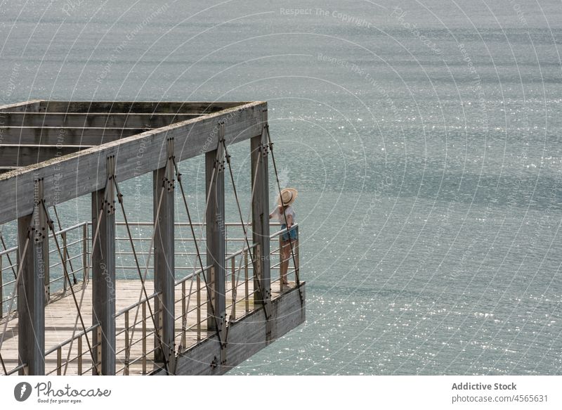 Frau sitzt auf Pier gegen ruhige See Tourist reisen beobachten hölzern Meereslandschaft Promenade Zaun Konstruktion Reling Cargadero da Insua Spanien Galicia