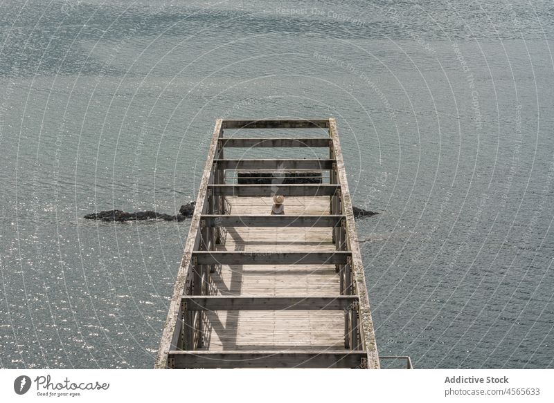 Frau sitzt auf Pier gegen ruhige See Tourist reisen beobachten hölzern Meereslandschaft Promenade Zaun Konstruktion Reling Cargadero da Insua Spanien Galicia