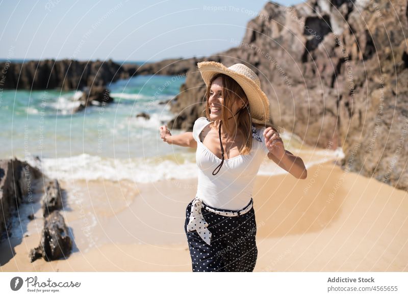Fröhliche Frau, die im Sommer am Sandstrand mit Klippen spazieren geht Strohhut Spanien Galicia praia furnas Strand Urlaub Spaziergang Feiertag Tourist