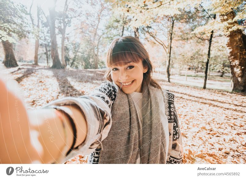 Happy girl using smart phone during Autumn in a park taking selfie, woman talking on mobile in fall. Videoanruf im Freien, gute Nachrichten erhalten. Person