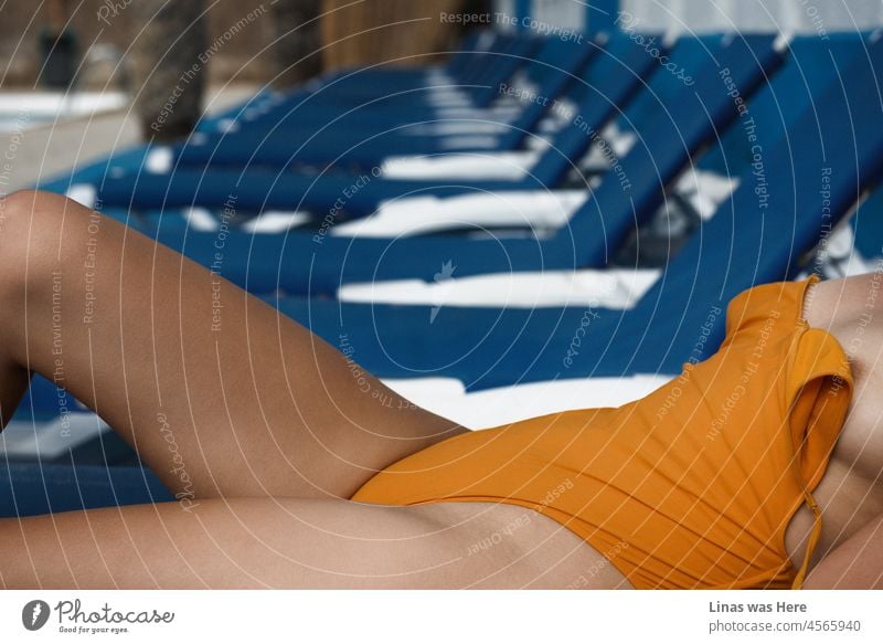 Ein Mädchen in einem orangefarbenen Badeanzug entspannt sich neben einem Swimmingpool. Es scheint im Moment ein leerer Ort zu sein. Nur ein wunderschönes Model, das eine gute Zeit mit ihren unbestreitbaren sexy Kurven vor der Kamera hat.