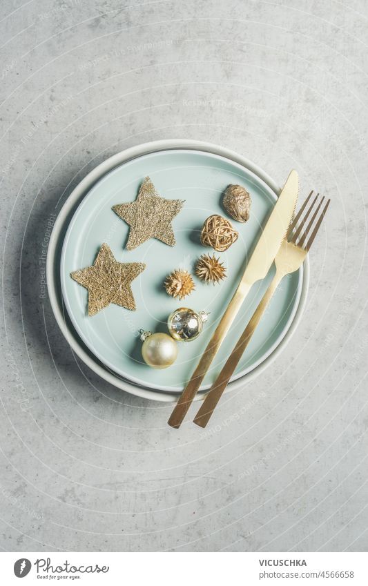 Weihnachtlich gedeckter Tisch mit goldenem Besteck, blassblauen Tellern, Dekoration mit Sternen und Kugeln auf grauem Betontisch. Festliches Abendessen. Ansicht von oben.