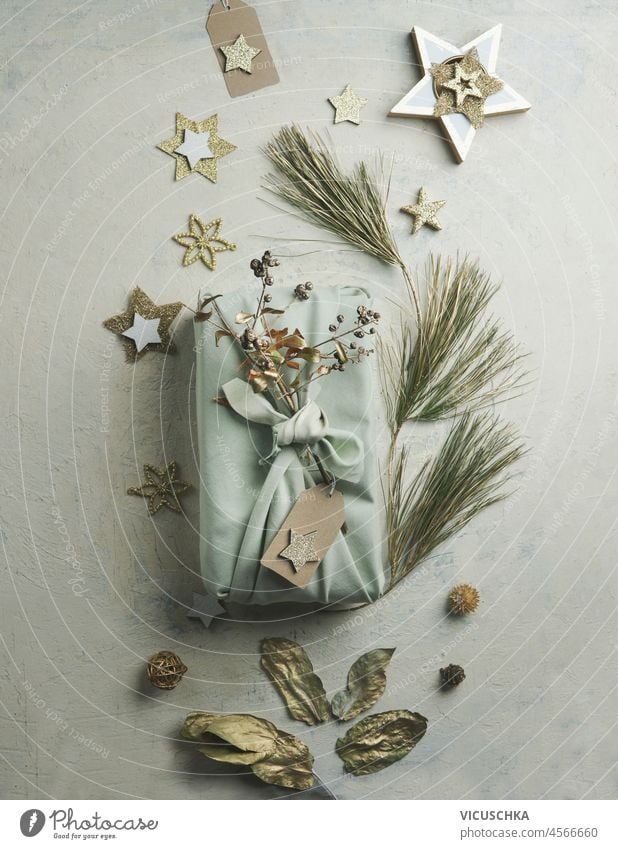 Umweltfreundliches Weihnachtsgeschenk, eingewickelt in Stoff mit goldenen Deko-Sternen, Zweige auf hellgrauem Tisch. Nachhaltige, abfallfreie Geschenkverpackung. Ansicht von oben.