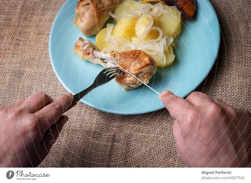 Frauenhände schneiden einen Zitronenhähnchenschenkel auf dem Teller, garniert mit Kartoffeln und Zwiebeln Hähnchen Oberschenkel Hände gekocht essen Ofen Speise