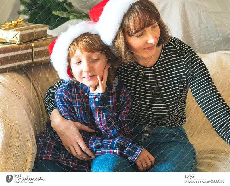 Mutter und Sohn in Weihnachtsmannmützen auf der Couch, Weihnachten Lifestyle Kind Familie wenig Dezember lässig Neujahr Zusammensein Verschlussdeckel umarmend