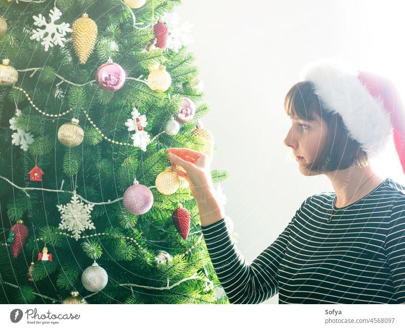 Frau in Weihnachtsmannmütze hält schmückenden Weihnachtsbaum, Urlaubsstimmung dekorieren Weihnachten Baum Ornament Christbaumkugeln heimwärts Kaukasier Dekor