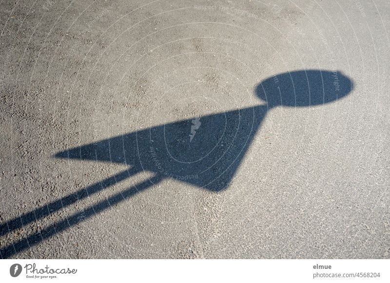 Schatten eines runden und eines dreieckigen Verkehrszeichens auf einer Asphaltstraße in Form eines Spielmännchens / optische Täuschung Verkehrsschild zwei
