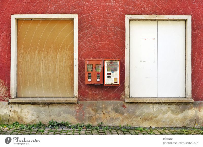 Zwei alte, defekte Kaugummiautomaten / Warenautomaten an einer rot verputzten Hauswand zwischen zwei mit Holz vernagelten Fenstern Verkaufsautomat marode kaputt