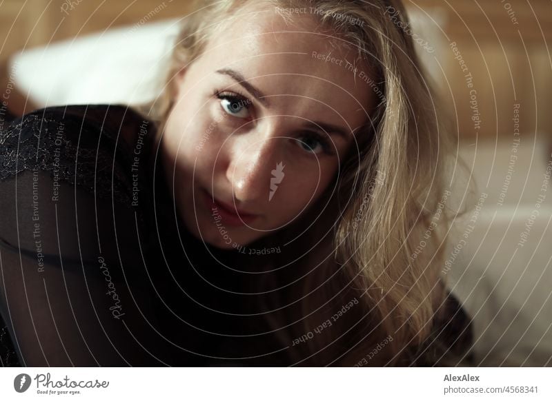 Portrait einer jungen, blonden, langhaarigen Frau, die im Bett liegend seitlich in die Kamera schaut Jugendlichkeit gesund Gesichtsausdruck Wärme drinnen