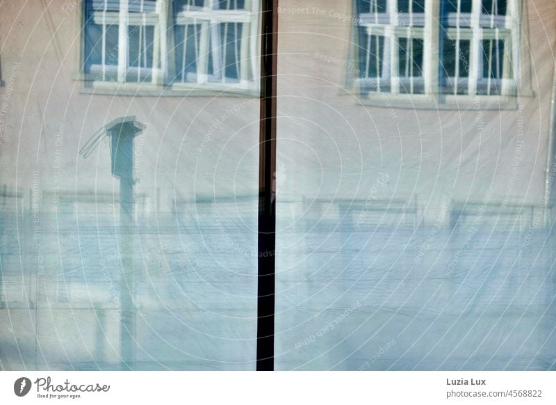 In den Fensterscheiben eines leerstehenden Straßencafés und dahinter hängenden Folien spiegelt sich die gegenüberliegende Fassade Glas Glasscheibe abhängt