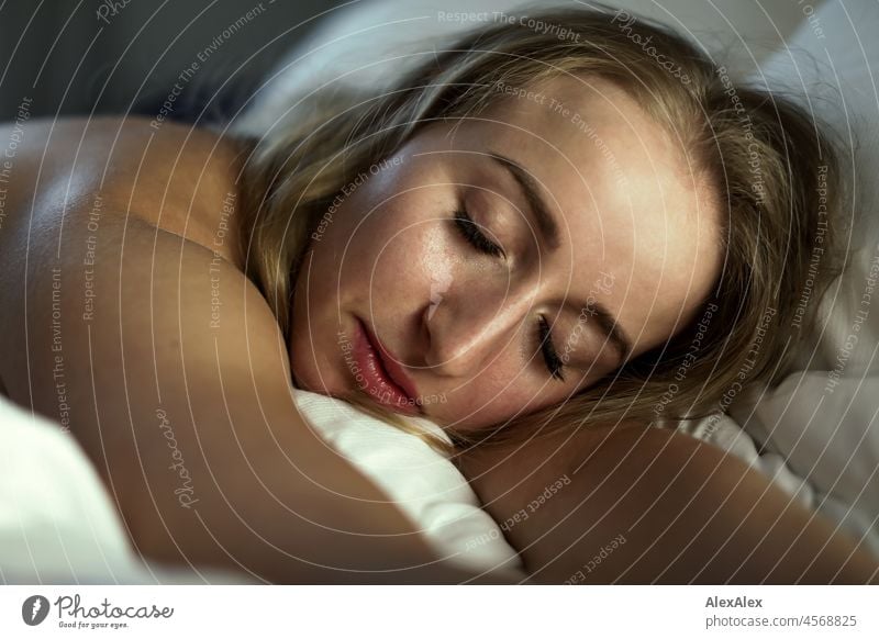 Aktportrait einer jungen, blonden, langhaarigen Frau, die scheinbar schlafend im Bett auf dem Bauch liegt Jugendlichkeit gesund Gesichtsausdruck Wärme drinnen