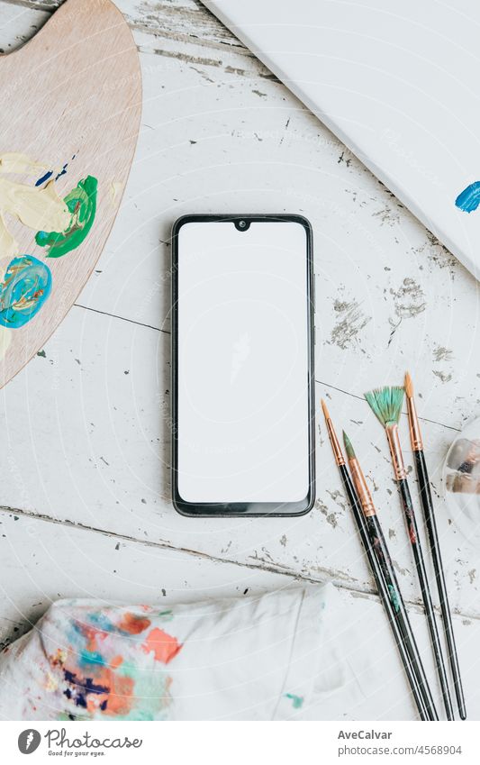 flache Pinsel mit einem Smartphone leeren Raum und Farbpalette mit viel Pigment auf einem weißen Holzhintergrund. Hobby Hintergrund. DIY, Handwerk Dekoration für Herbstferien. Flachlage, Draufsicht