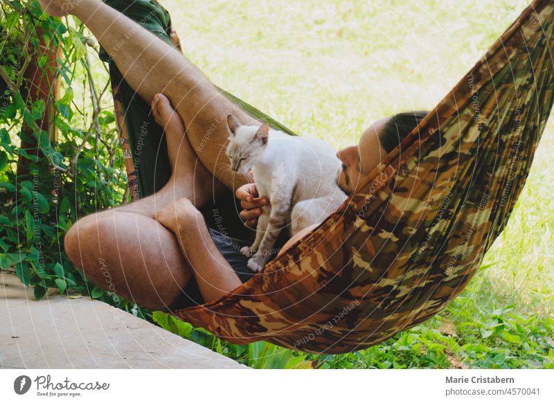 Ein Mann entspannt sich in der Hängematte mit seiner Siamesischen Katze 30-34 Jahre alt Freizeit Tierhalter siamesische Katze Zusammengehörigkeitsgefühl bequem