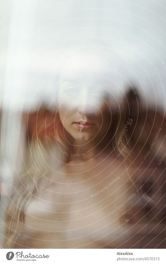 Aktportrait einer jungen, blonden, langhaarigen Frau, die hinter der Fensterscheibe nackt in die Kamera schaut Jugendlichkeit gesund Gesichtsausdruck Wärme