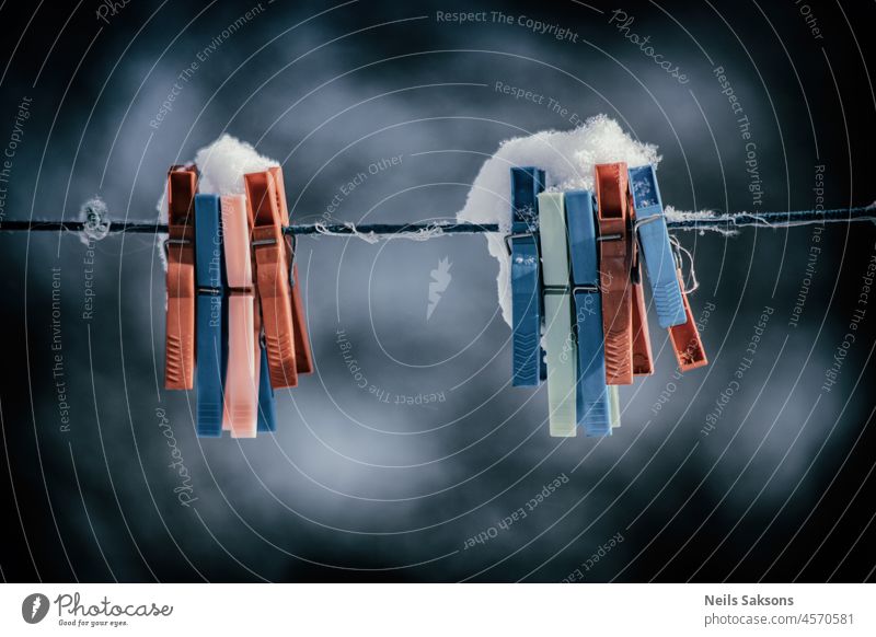 Bunte Wäscheklammern auf Wäscheleine mit Schnee bedeckt im Freien. Winterszene, Hausarbeit Konzept Hintergrund blau einklemmen Clip Nahaufnahme Kleidung