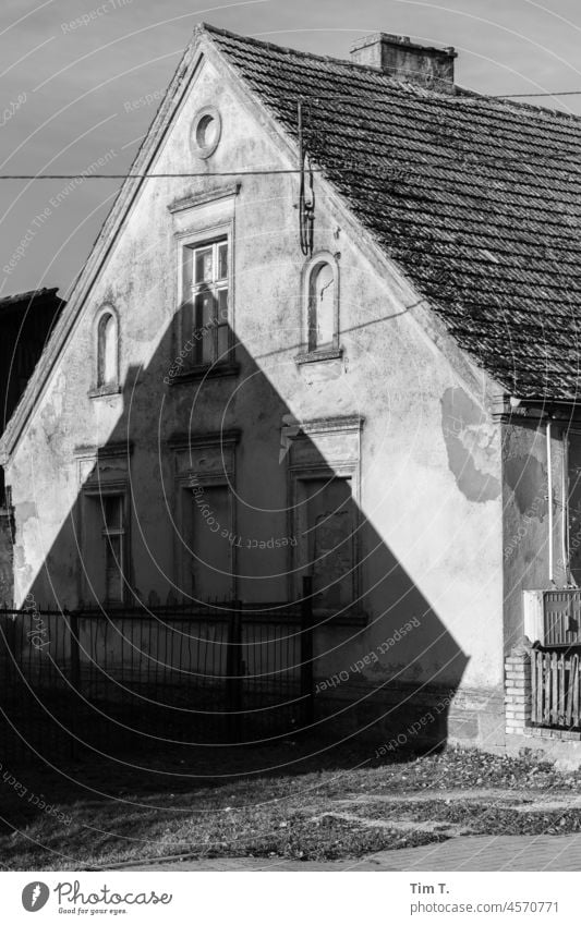 der Giebel eines alten Hauses wirft einen Schatten auf ein anderes altes Haus Dorf altes haus Giebelseite s/w bnw Polen Winter Tag Schwarzweißfoto Menschenleer