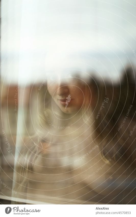 Aktportrait einer jungen, blonden, langhaarigen Frau, die hinter der Fensterscheibe nackt in die Kamera schaut Jugendlichkeit gesund Gesichtsausdruck Wärme