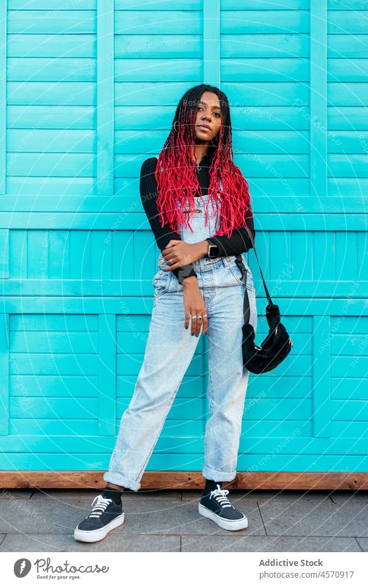 Schwarze Frau steht auf der Straße in der Nähe der blauen Wand Afro-Zöpfe Individualität Frisur Vorschein Persönlichkeit Outfit Stil trendy ethnisch Großstadt