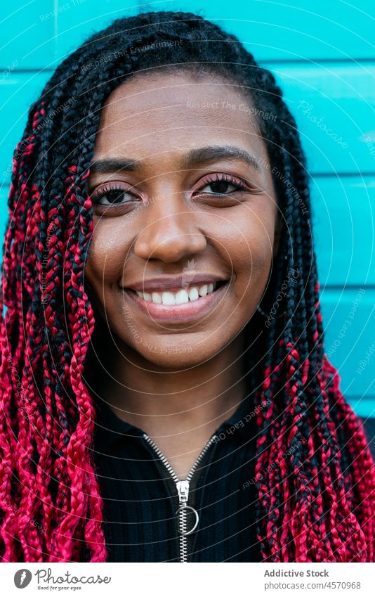 Afroamerikanische Frau steht auf blauer Wand Porträt Menschliches Gesicht Model Inhalt Glück Lächeln Frisur Afro-Zöpfe Vorschein Individualität Stil jung trendy