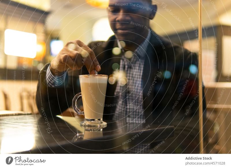 Crop schwarzer Mann rührt Latte Macchiato in Cafeteria rühren Mokka Kaffee Café Lächeln elegant trinken Fenster Kaffeepause Heißgetränk Geschäftsmann männlich