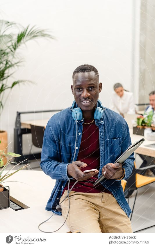 Fröhlicher schwarzer Mann, der in der Nähe von Kollegen auf seinem Smartphone surft Geschäftsleute Browsen Arbeit online Mitarbeiterin Büro Unternehmen Tablette