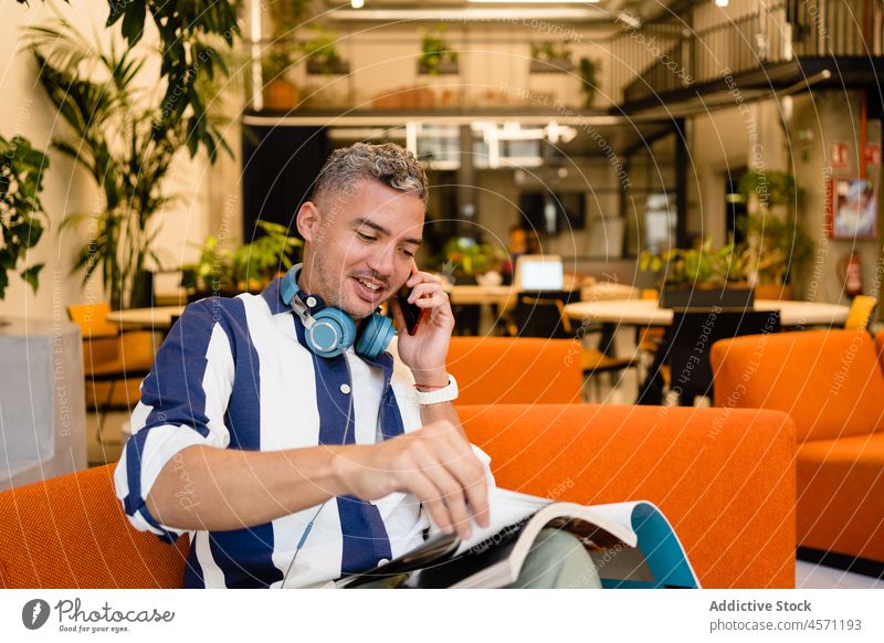 Mann liest eine Zeitschrift, während er im Büro telefoniert Smartphone Telefonanruf Gespräch Magazin lesen Kommunizieren Arbeit Arbeiter benutzend Apparatur