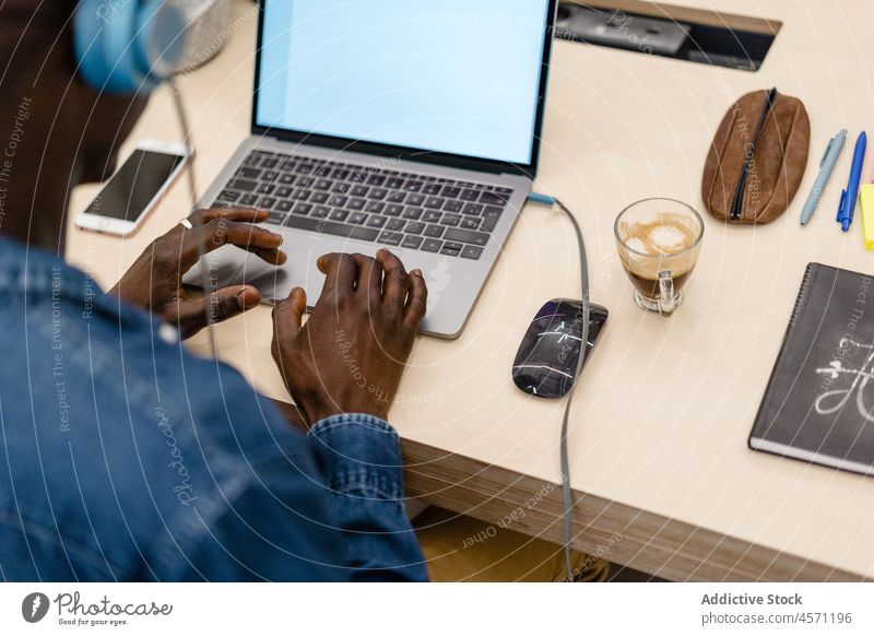 Anonymer schwarzer Mann mit Kopfhörern arbeitet an einem Laptop Musik Büro Tippen Internet online Arbeit Browsen Arbeiter benutzend Apparatur Gerät zuhören