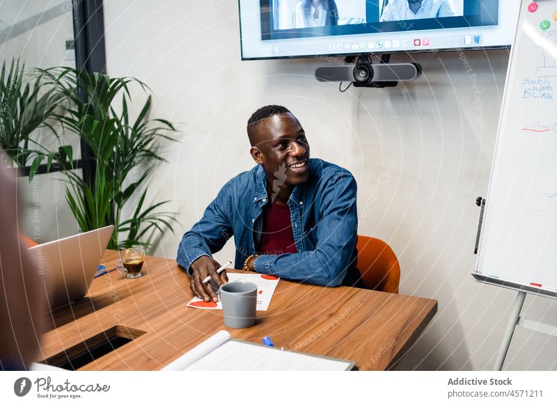 Fröhlicher schwarzer Mann sitzt am Tisch im Büro Arbeit Arbeiter Unternehmen Mitarbeiter Papierkram Schriftstück Arbeitsplatz Beruf männlich Arbeitsbereich