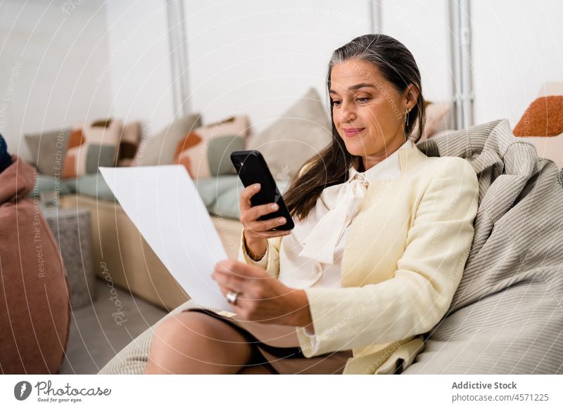 Frau mit Dokumenten beim Surfen auf dem Smartphone Schriftstück Papierkram Arbeit Büro Arbeiter analysieren Unternehmen Mitarbeiter Arbeitsplatz Arbeitsbereich