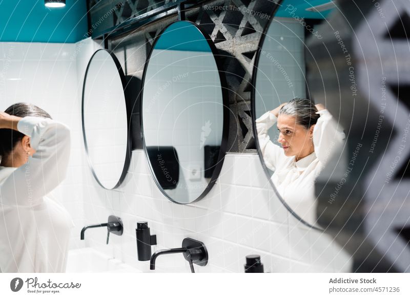 Frau, die sich in der Nähe des Spiegels auf der Toilette frisiert Frisur Pferdeschwanz Reflexion & Spiegelung Stil fixieren modern Waschbecken Sauberkeit Outfit
