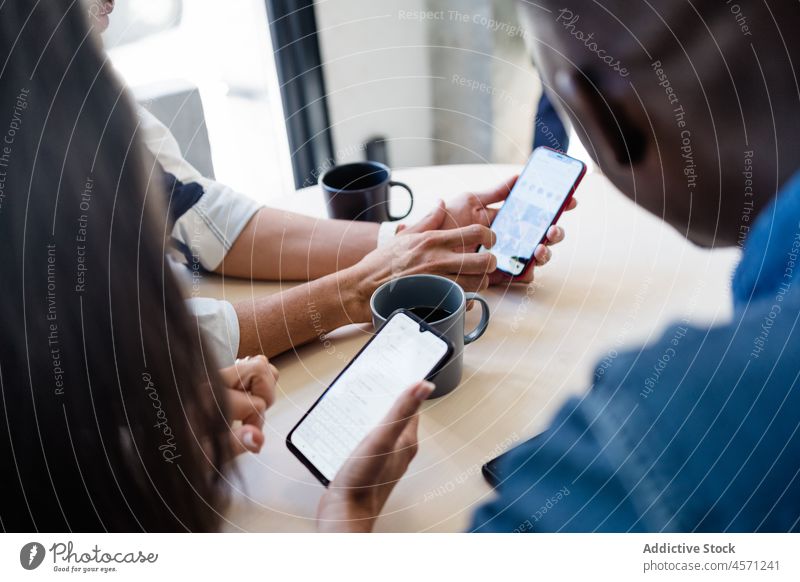 Anonyme multiethnische Kollegen, die in einem Café mit ihren Smartphones surfen Geschäftsleute Browsen online Kaffeepause Heißgetränk Mitarbeiterin Anschluss