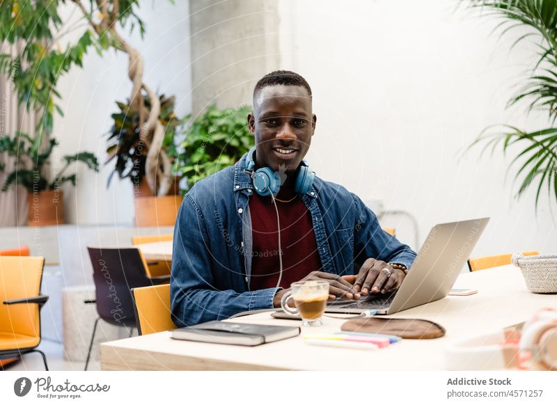 Schwarzer Mann mit Kopfhörern arbeitet an einem Laptop Büro Tippen Internet online Arbeit Browsen Arbeiter benutzend Apparatur Gerät Netbook Kaffee Mitarbeiter