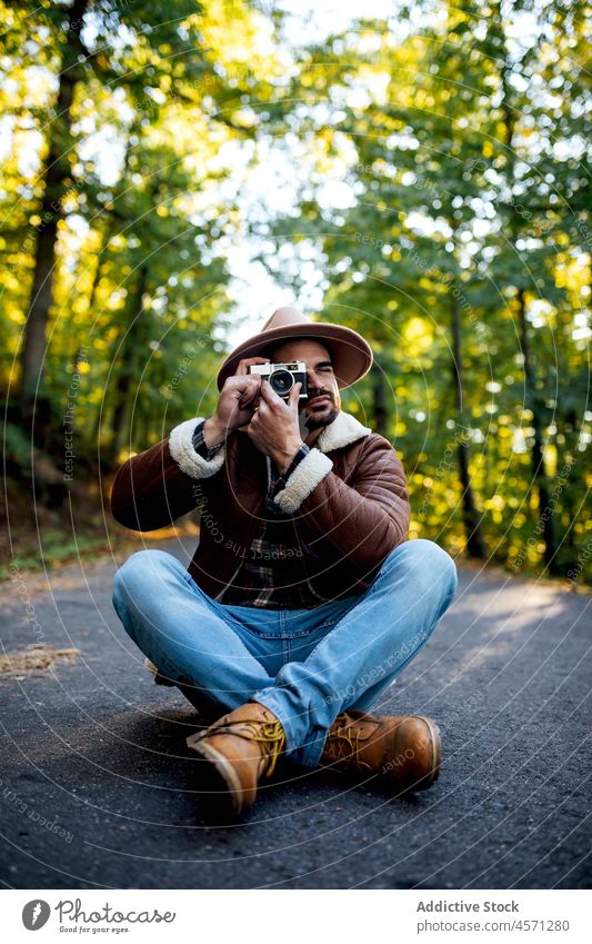 Mann fotografiert auf der Straße sitzend Baum Weg Fotoapparat fotografieren Fotograf Natur Hain Erholung Stil Porträt Abenteuer Ausflug Freizeit Outfit trendy