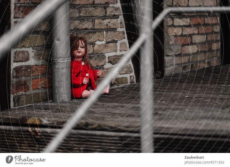 Rot gekleidete Puppe sitzt verloren auf Holzboden mit Geländer sitzen Angst rot Holzbohlen Fachwerk Ziegel Kindheit Verlust Versteck Einsamkeit Spielzeug