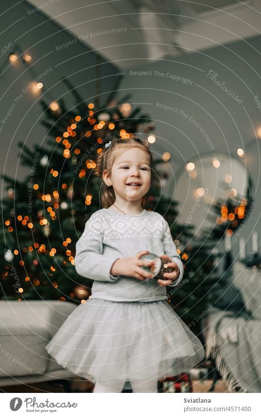 Ein hübsches kleines Mädchen in einem festlichen Kleid steht am Weihnachtsbaum. das Konzept von Weihnachten und Neujahr wenig schön Baum Feiertag