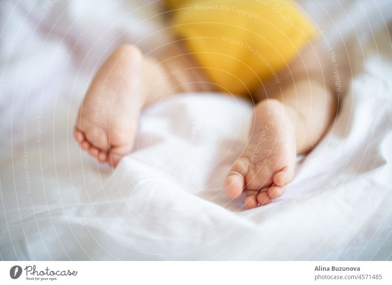 Baby's Füße Nahaufnahme. Caucasian Baby sieben Monate alt schlafen auf dem Bett zu Hause. Kind trägt niedliche Kleidung gelbe Farbe neugeboren Säugling