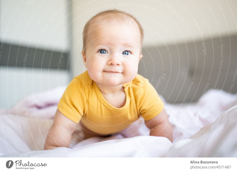 Kaukasische blonde Baby sieben Monate alt auf dem Bett zu Hause liegen. Kind trägt niedliche Kleidung gelbe Farbe neugeboren Säugling lichtvoll ultimativ grau
