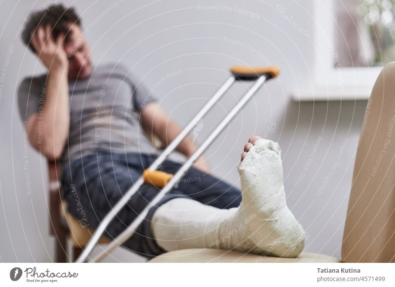 Ein Mann mit einem gebrochenen Bein und Krücken sitzt da und fasst sich an den Kopf. Fokus auf den Fuß Menschen weiß Kaukasier grün gießen Person Erwachsener 1