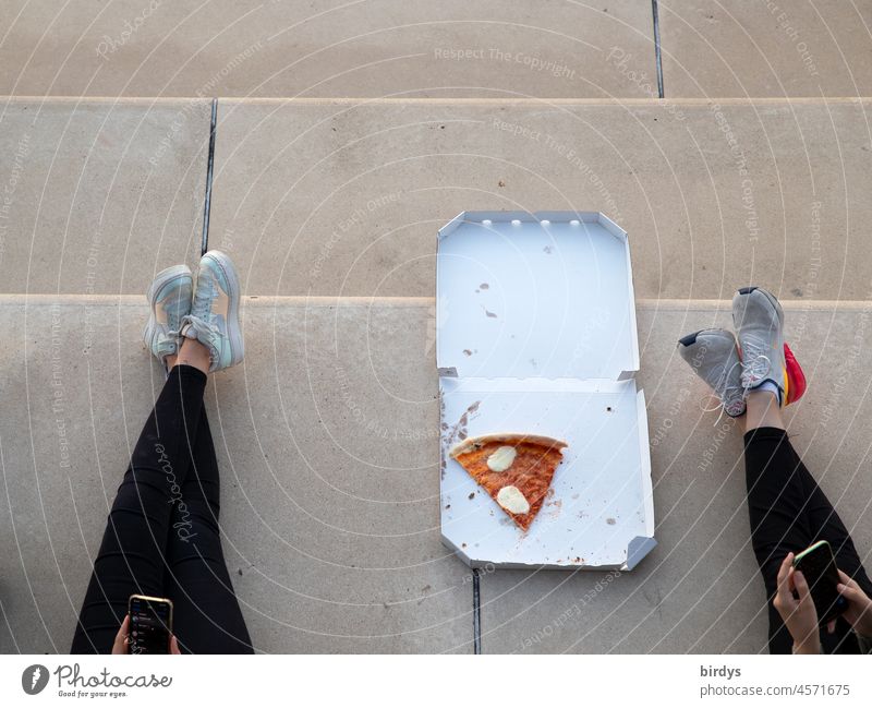 Pizza to go. Jugendliche Mädchen spielen am smartphone und essen Pizza im Freien. Vogelperspektive Smartphone Pizzaschachtel freizeit zusammen sneakers