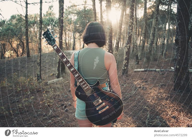 Rückenansicht eines jungen Hipster Frau spielt die Gitarre lächelnd außerhalb des Waldes Park der Stadt. Mit Spaß lernen eine neue Fähigkeit, Musik spielen saisonalen Stil. Junge kurze Haare Mädchen. Kopieren Raum