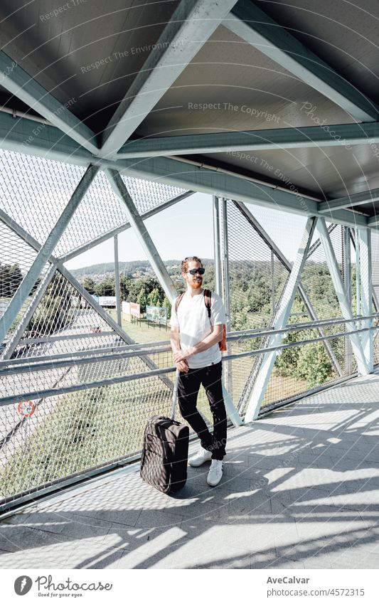 Porträt eines jungen Mannes auf dem Flughafen oder Busbahnhof, Gepäck, Taschen und Koffer. Lächelnder Hipster-Reisender mit Sonnenbrille, Kopierraum, sonniger Tag