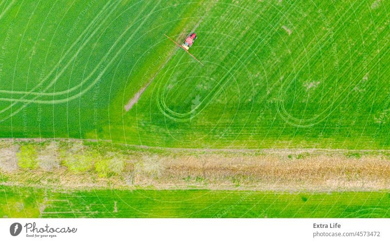Luftaufnahme eines Traktors beim Besprühen eines Feldes mit jungen Getreidekulturen mit Sprühgerät, Herbizid und Pestizid oben Aerosol landwirtschaftlich