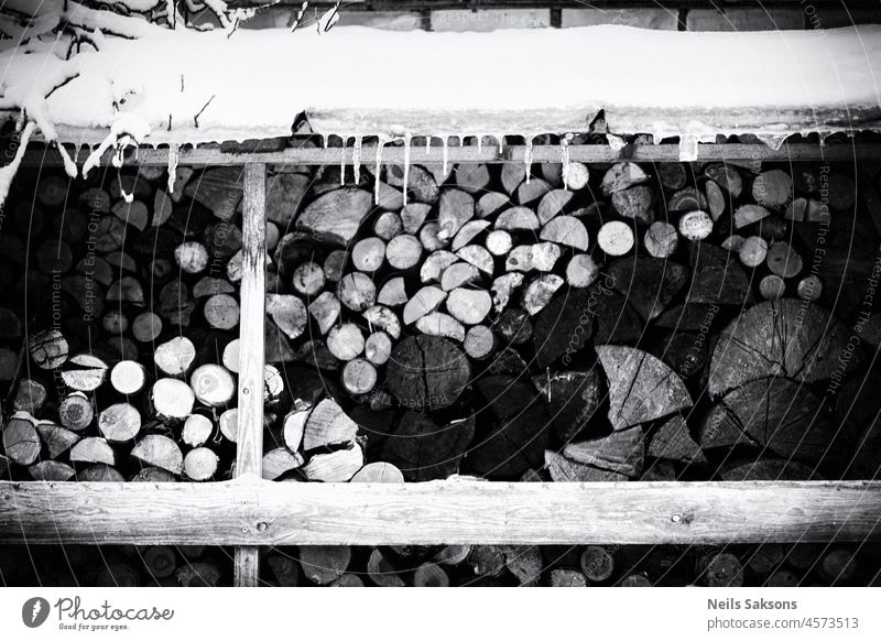 Brennholz im Winter unter verschneitem Dach, Eiszapfen, schwarz-weiß monochrom Hintergrund Ast braun gehackt kalt Farbe bedeckt geschnitten Energie Umwelt Feuer